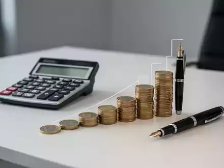 Ein Taschenrechner und Euro-Münzen auf einem Schreibtisch, die eine steigende Grafik bilden, symbolisch für Sozialversicherungsbeiträge. - Foto: über boerse-global.de