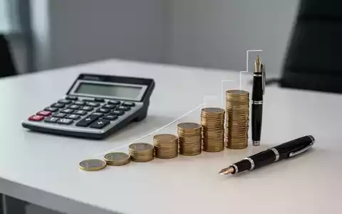 Ein Taschenrechner und Euro-Münzen auf einem Schreibtisch, die eine steigende Grafik bilden, symbolisch für Sozialversicherungsbeiträge. - Foto: über boerse-global.de