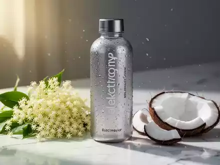 Eine Flasche Elektrolytgetränk mit Holunderblüten und Kokosnussstücken auf einer Marmoroberfläche bei sommerlichem Licht. - Foto: über boerse-global.de