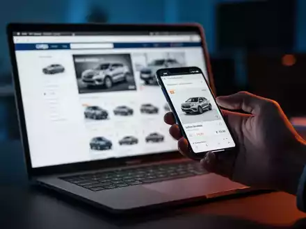 Ein Laptop mit einer Autoverkaufsplattform neben einem Smartphone, das die Gefahr von Online-Betrug bei Autokäufen symbolisiert. - Foto: über boerse-global.de