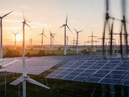 Moderne Windkraftanlagen und Solarparks in einer deutschen Landschaft bei Sonnenaufgang mit Strommasten im Hintergrund. - Foto: über boerse-global.de