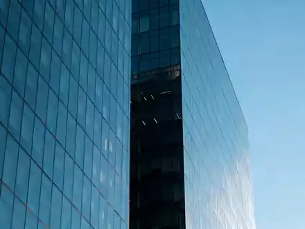 Ein modernes Bürogebäude spiegelt sich in einer Glasfassade bei klarem Himmel. - Foto: über boerse-global.de