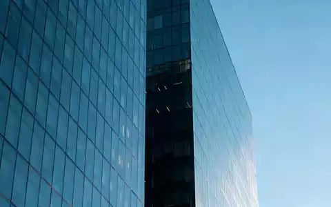 Ein modernes Bürogebäude spiegelt sich in einer Glasfassade bei klarem Himmel. - Foto: über boerse-global.de