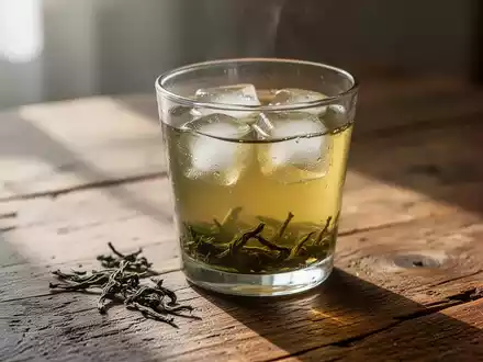 Ein Glas mit kaltem Grüntee und Eiswürfeln auf einem Holztisch bei natürlichem Tageslicht. - Foto: über boerse-global.de