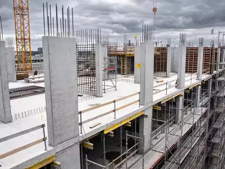 Eine unfertige Baustelle mit Baukränen und Gerüsten vor einem bewölkten Himmel. - Foto: über boerse-global.de