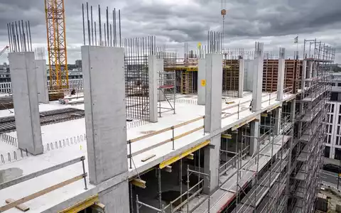 Eine unfertige Baustelle mit Baukränen und Gerüsten vor einem bewölkten Himmel. - Foto: über boerse-global.de