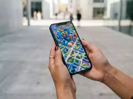 Person hält ein modernes Smartphone mit einer detaillierten 3D-Kartenansicht in einer urbanen Umgebung. - Foto: über boerse-global.de