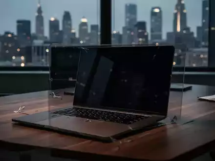 Ein unbesetzter, modern eingerichteter Arbeitsplatz mit einem Laptop, dessen Bildschirm dunkel bleibt, wĂ€hrend im Hintergrund eine verschwommene Stadtkulisse zu sehen ist. - Foto: ĂŒber boerse-global.de
