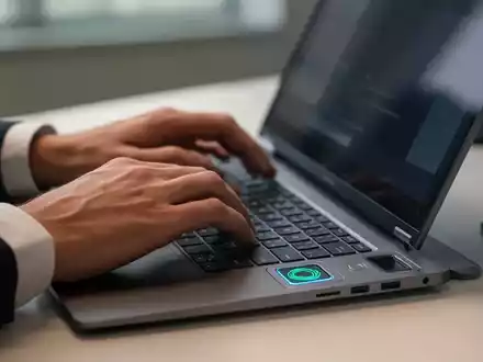Person an einem Laptop mit integriertem biometrischem Fingerabdruckscanner zur Authentifizierung in einer Büroumgebung. - Foto: über boerse-global.de