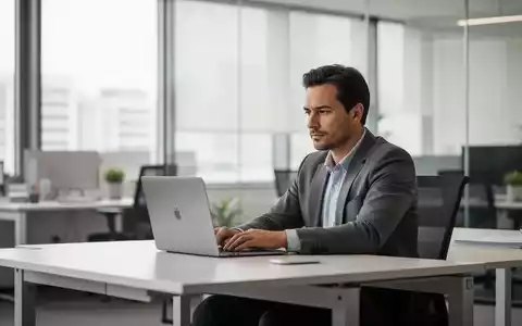 Ein Angestellter sitzt an einem aufgeräumten Schreibtisch vor einem Laptop in einem modernen, hellen Büro. - Foto: über boerse-global.de