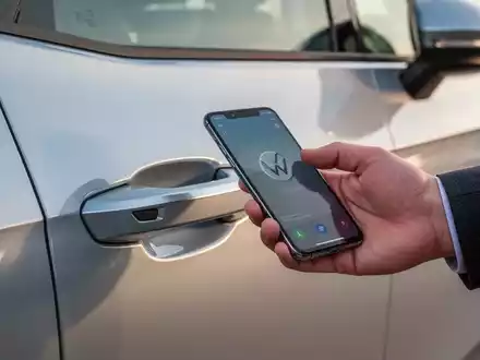 Eine Hand hält ein Smartphone nahe an den Türgriff eines modernen Volkswagen ID.3 Neo Elektroautos. - Foto: über boerse-global.de