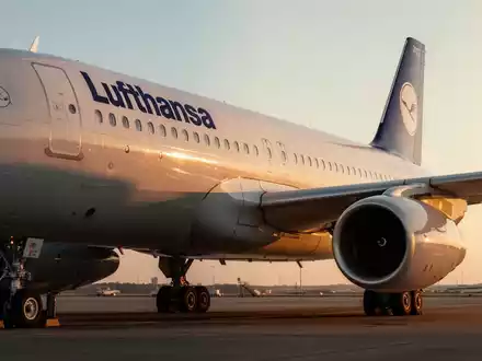 Ein Lufthansa-Flugzeug auf dem Rollfeld eines Flughafens bei Sonnenuntergang. - Foto: über boerse-global.de