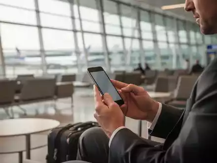Ein Geschäftsmann nutzt in einer modernen Flughafen-Lounge sein Smartphone zur sicheren digitalen Kommunikation. - Foto: über boerse-global.de
