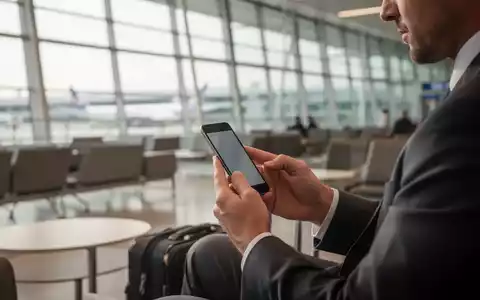 Ein Geschäftsmann nutzt in einer modernen Flughafen-Lounge sein Smartphone zur sicheren digitalen Kommunikation. - Foto: über boerse-global.de