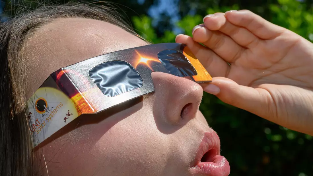 Eine junge Frau schaut durch eine Sonnenfinsternisbrille und betrachtet die Mittagssonne. - Bild: Patrick Pleul/dpa