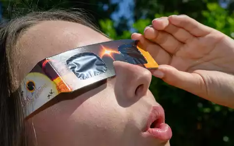 Eine junge Frau schaut durch eine Sonnenfinsternisbrille und betrachtet die Mittagssonne. - Foto: Patrick Pleul/dpa