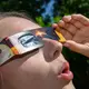 Eine junge Frau schaut durch eine Sonnenfinsternisbrille und betrachtet die Mittagssonne. - Bild: Patrick Pleul/dpa
