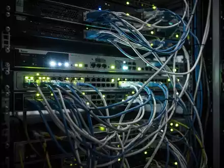 Dunkler Serverraum mit leuchtenden Netzwerkkabeln und technischer Infrastruktur. - Foto: über boerse-global.de