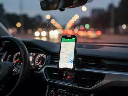 Ein Smartphone mit Navigations-App in einer Autohalterung bei Dämmerung, während das Fahrzeug auf einer beleuchteten Straße fährt. - Foto: über boerse-global.de
