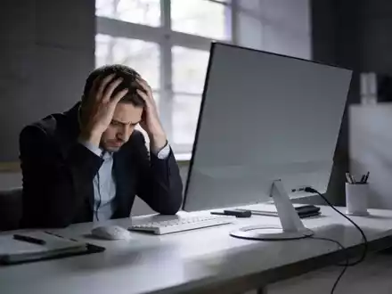 Ein besorgter Büroangestellter sitzt an einem Schreibtisch vor einem leeren Bildschirm in einem modernen Büro. - Foto: über boerse-global.de