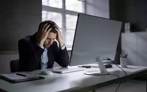 Ein besorgter Büroangestellter sitzt an einem Schreibtisch vor einem leeren Bildschirm in einem modernen Büro. - Foto: über boerse-global.de
