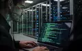 Ein Cybersecurity-Analyst arbeitet in einem modern beleuchteten Serverraum an einem Laptop mit komplexen Datenvisualisierungen. - Foto: über boerse-global.de