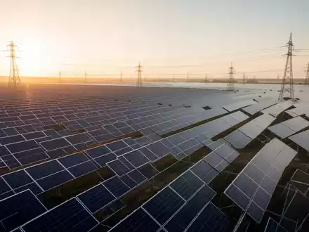 Weitläufiger Solarpark bei Sonnenaufgang mit Photovoltaik-Modulen und Strommasten in der Ferne. - Foto: über boerse-global.de