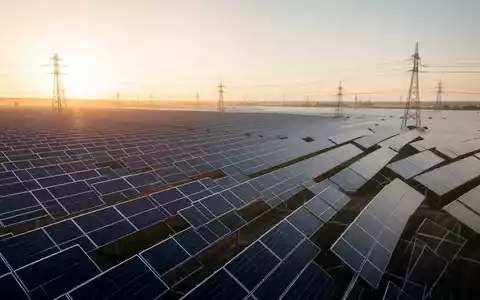 Weitläufiger Solarpark bei Sonnenaufgang mit Photovoltaik-Modulen und Strommasten in der Ferne. - Foto: über boerse-global.de