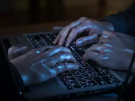 Nahaufnahme einer Person, die in einem abgedunkelten Raum an einem Laptop arbeitet, beleuchtet durch das Licht des Bildschirms. - Foto: über boerse-global.de