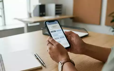 Hände einer Lehrperson halten ein Smartphone in einer hellen Büroumgebung während einer Schulung zur digitalen Sicherheit. - Foto: über boerse-global.de