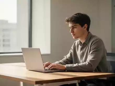 Eine junge Person sitzt nachdenklich vor einem Laptop in einem modernen, hellen Büro. - Foto: über boerse-global.de