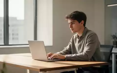 Eine junge Person sitzt nachdenklich vor einem Laptop in einem modernen, hellen Büro. - Foto: über boerse-global.de