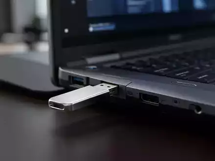 Nahaufnahme eines USB-Sticks, der in den Anschluss eines Business-Laptops eingesteckt wird, in einer Büroumgebung. - Foto: über boerse-global.de
