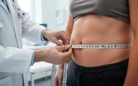 Ein Arzt misst in einer modernen medizinischen Praxis den Taillenumfang eines Patienten mit einem Maßband. - Foto: über boerse-global.de