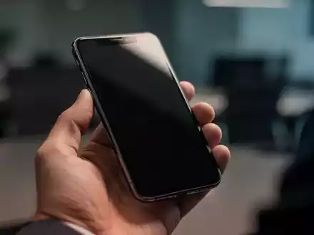 Nahaufnahme einer Person, die ein Smartphone in einer professionellen Büroumgebung prüft. - Foto: über boerse-global.de