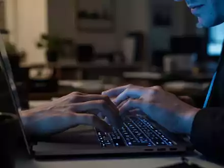 Nahaufnahme einer Person an einem Laptop in einem abgedunkelten Raum, die an ihre digitale Sicherheit denkt. - Foto: über boerse-global.de