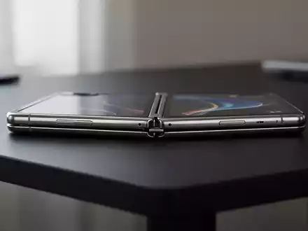 Ein faltbares Smartphone mit einem schlanken Metallgehäuse liegt auf einem schlichten, dunklen Tisch. - Foto: über boerse-global.de