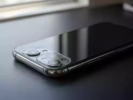 Ein modernes Smartphone liegt auf einem dunklen Schreibtisch, beleuchtet durch weiches, natürliches Licht. - Foto: über boerse-global.de