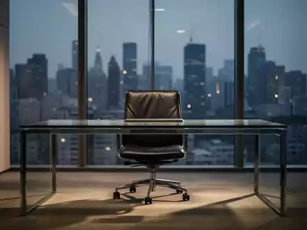 Ein leerer Bürostuhl hinter einem Schreibtisch in einer modernen, lichtdurchfluteten Führungsetage während der Dämmerung. - Foto: über boerse-global.de