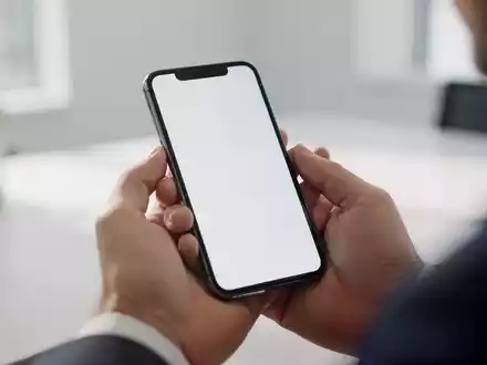 Nahaufnahme einer Hand, die ein Smartphone in einer hellen Büroumgebung hält. - Foto: über boerse-global.de