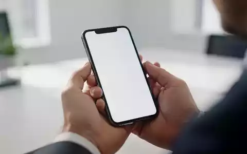 Nahaufnahme einer Hand, die ein Smartphone in einer hellen Büroumgebung hält. - Foto: über boerse-global.de