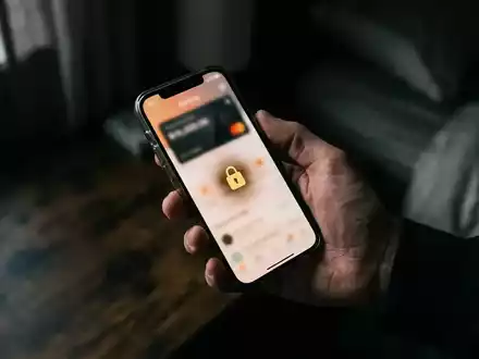 Nahaufnahme einer Hand, die ein Smartphone mit unscharfer Banking-App in einem abgedunkelten Raum hält. - Foto: über boerse-global.de