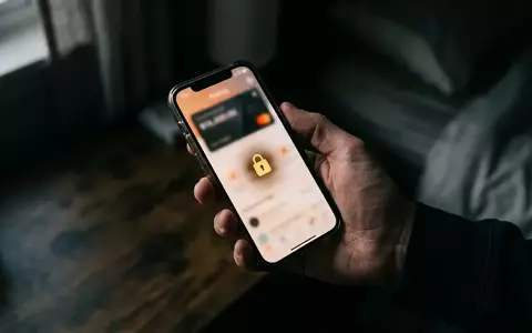 Nahaufnahme einer Hand, die ein Smartphone mit unscharfer Banking-App in einem abgedunkelten Raum hält. - Foto: über boerse-global.de