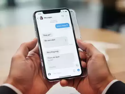 Nahaufnahme einer Hand, die ein Smartphone hält, auf dessen Display eine Nachrichten-App mit Chatverlauf zu sehen ist. - Foto: über boerse-global.de