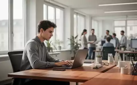 Ein junger Fachmann arbeitet in einem modernen, hellen Büro an einem Laptop, während Kollegen im Hintergrund diskutieren. - Foto: über boerse-global.de