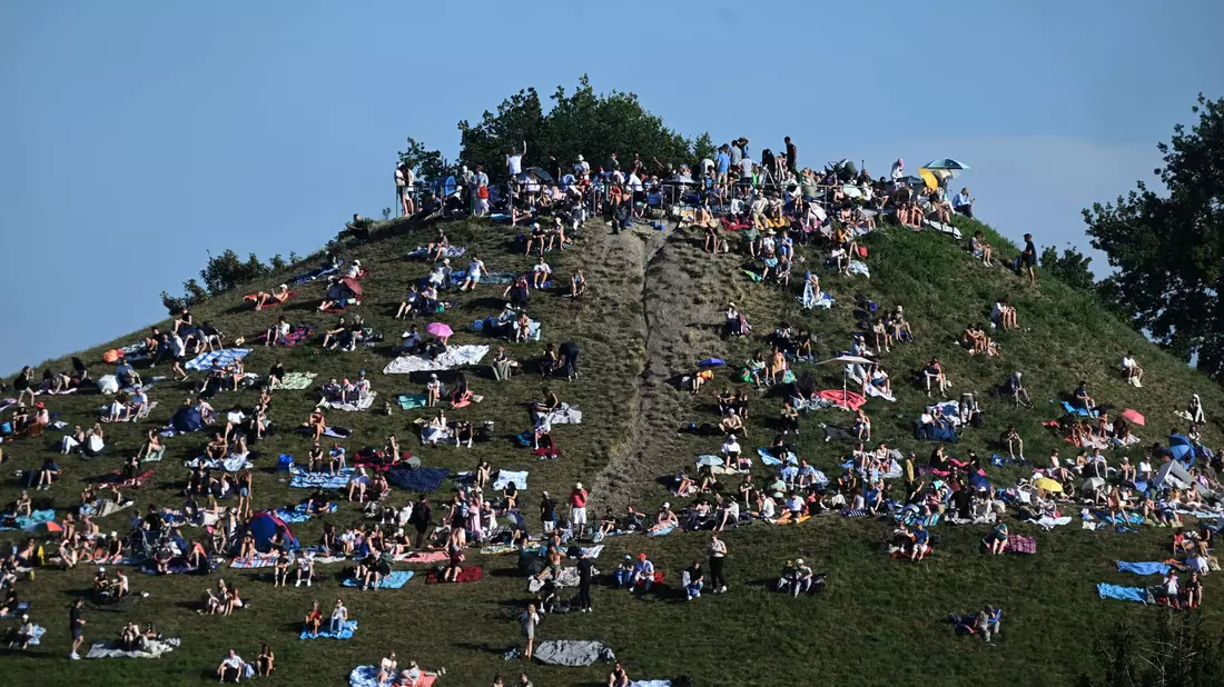 Erste Besucher bevölkern den Olympiaberg im Münchner Olympiapark, um von dort die partielle Sonnenfinsternis zu beobachten. - Bild: Felix Hörhager/dpa