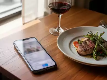 Ein Smartphone auf einem Restauranttisch neben einem Teller mit Essen, das zur Reservierung genutzt wird. - Foto: über boerse-global.de