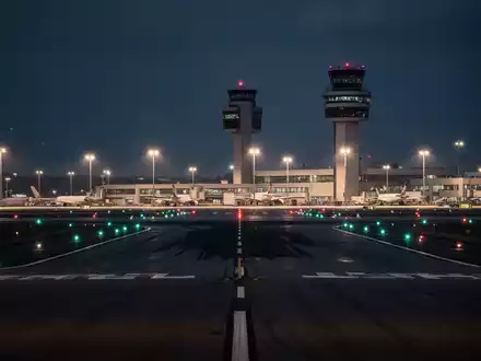 Ein nächtlicher Blick auf die Rollbahnen eines Verkehrsflughafens mit beleuchtetem Tower in der Ferne. - Foto: über boerse-global.de