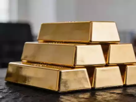 Goldbarren auf einem dunklen Untergrund gestapelt, beleuchtet durch weiches, natürliches Licht. - Foto: über boerse-global.de
