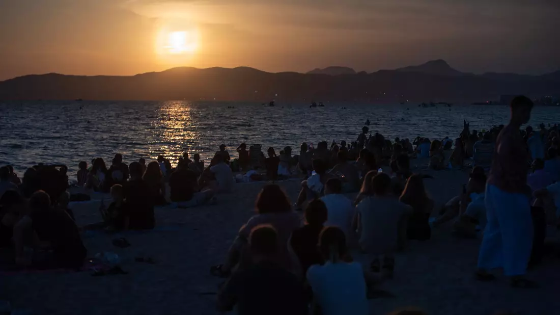 Menschen sitzen am Strand von Palma und warten auf die totale Sonnenfinsternis. - Bild: Clara Margais/dpa